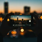 Pessoa fotografando uma paisagem urbana noturna com um iPhone, demonstrando a capacidade de captura em pouca luz.