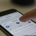 Configurações de Wi-Fi e Bluetooth na tela de um iPhone, com uma mão tocando o dispositivo.